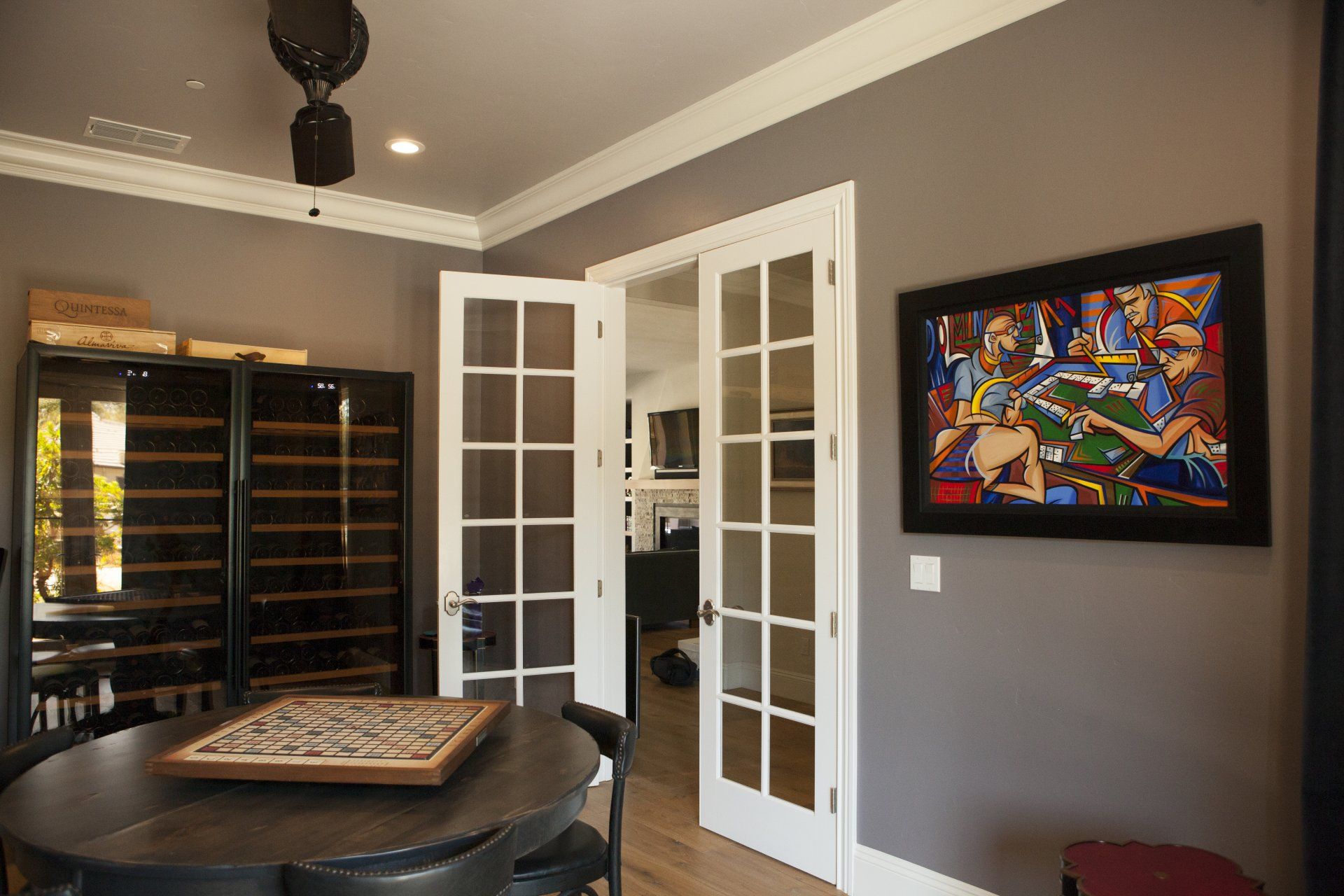 Room with gray walls, French doors, wine storage, round table, and colorful artwork.