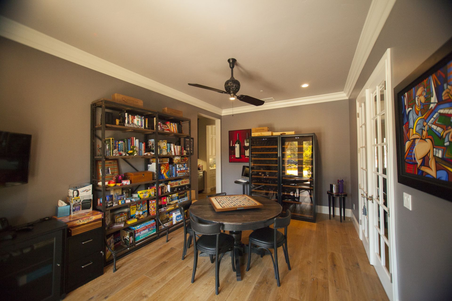 A home game room with a round table, bookshelves, a wine rack, and a dark ceiling fan.