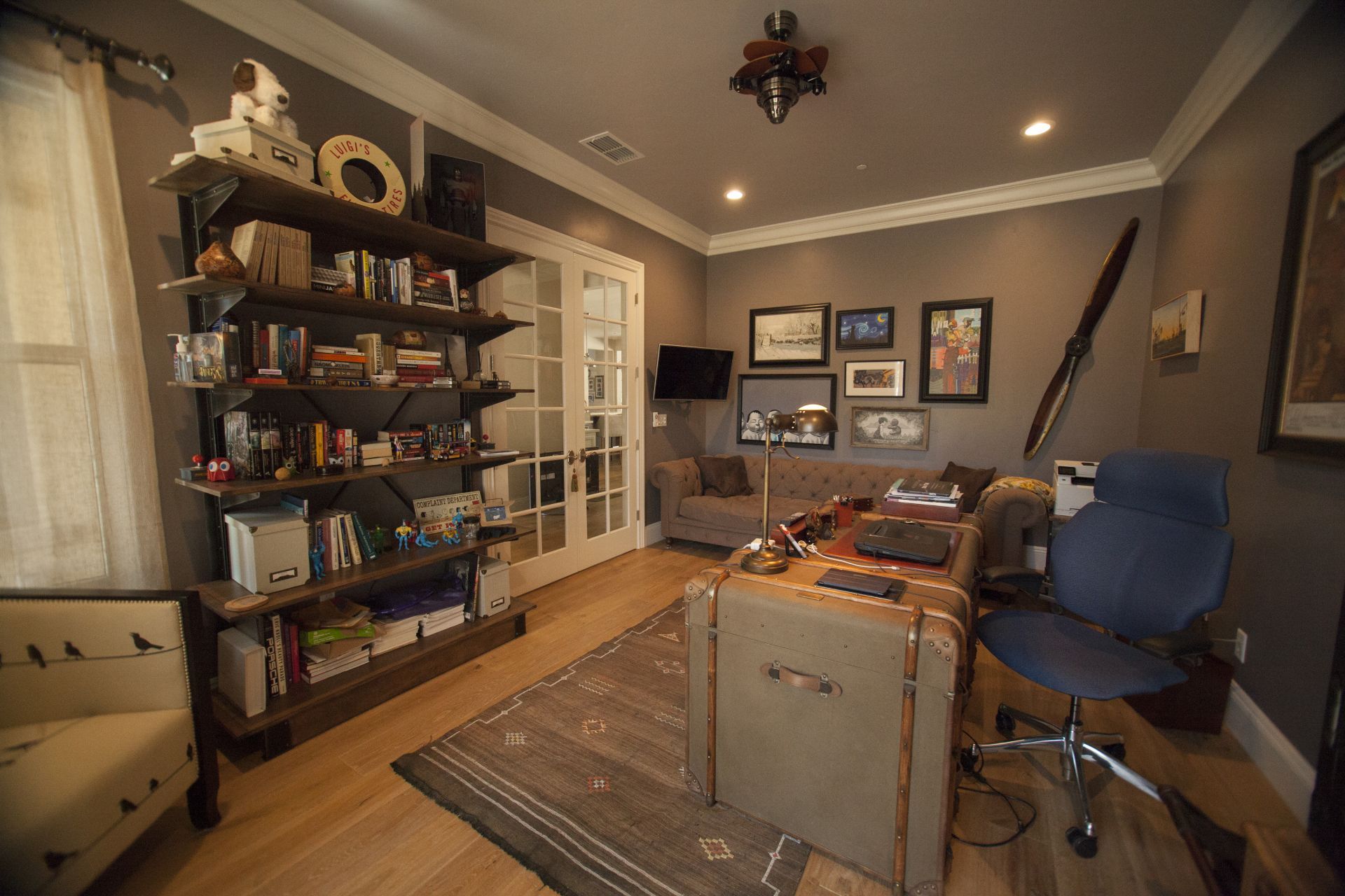 Home office with shelves, desk, and sitting area. The room is painted gray with wood flooring.