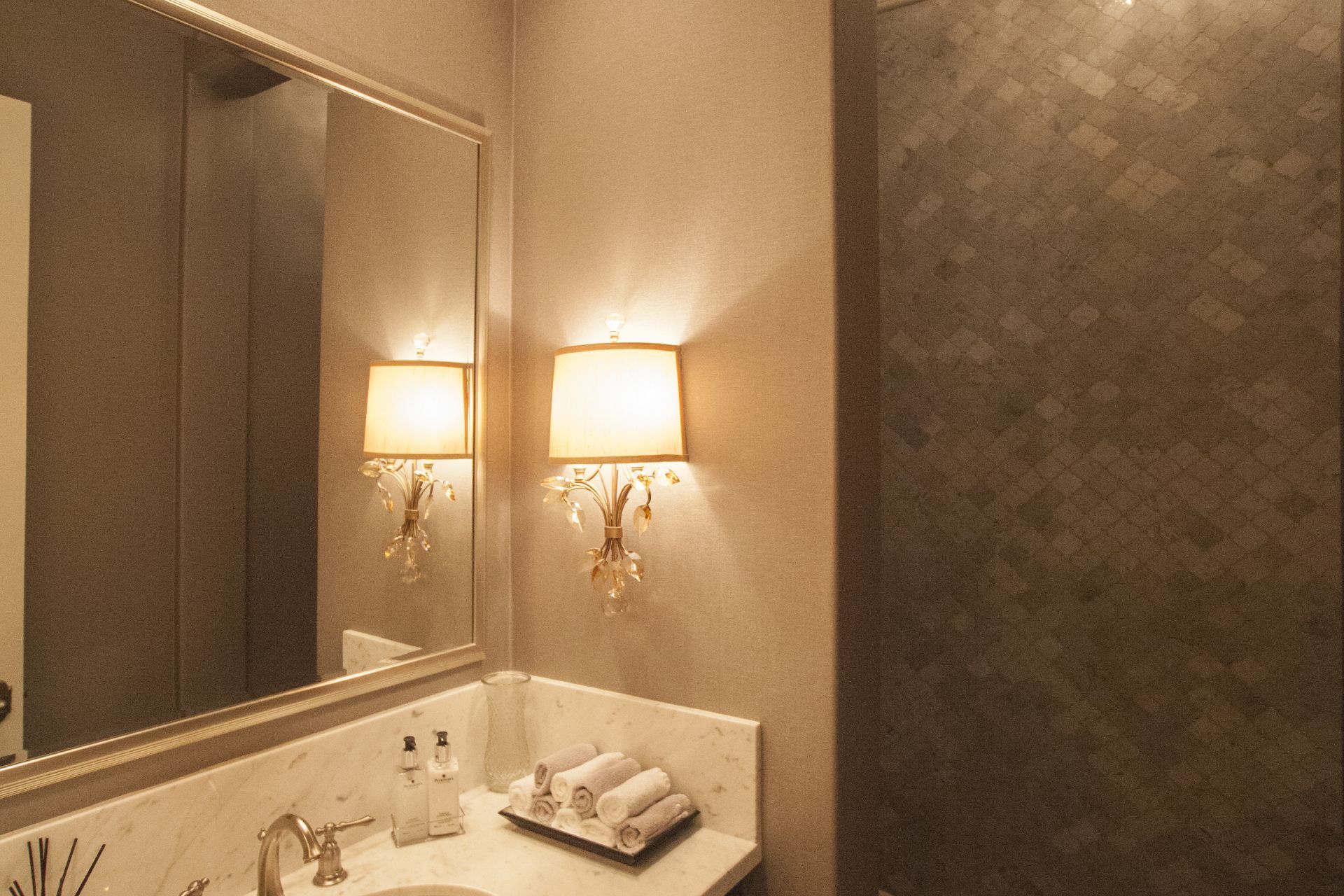 A luxurious bathroom with a marble countertop, ornate sconces, and a decorative tile accent wall.