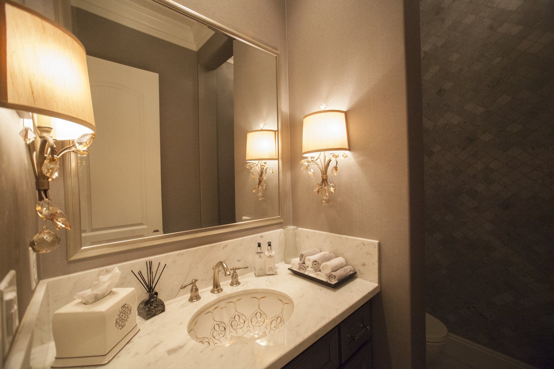 Bathroom with a white marble vanity, ornate mirror, sconces, and neutral walls.