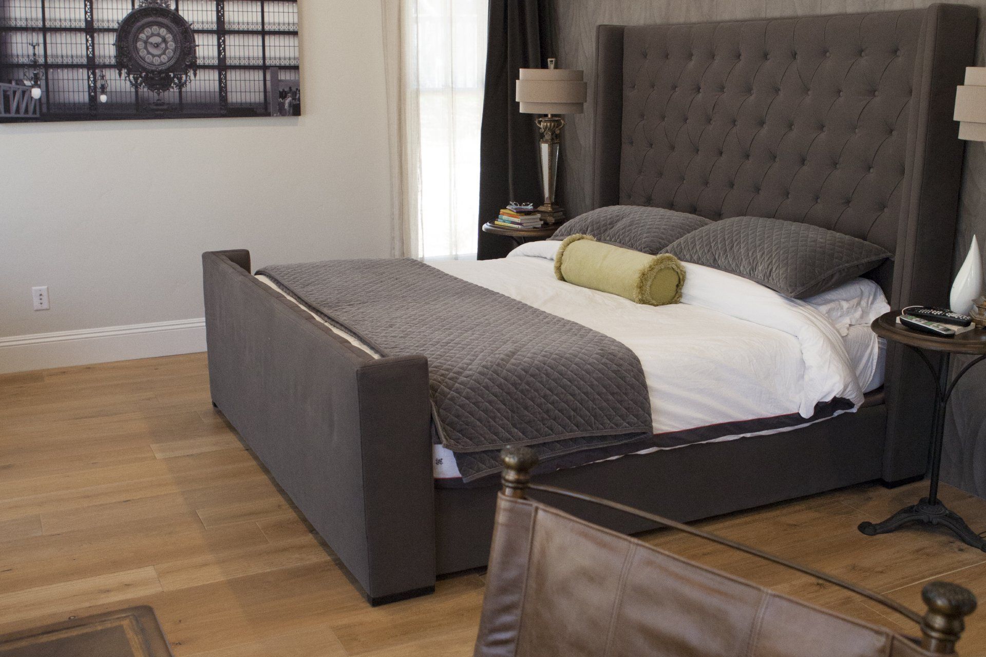 Gray upholstered bed in a modern bedroom with artwork and wooden floors.