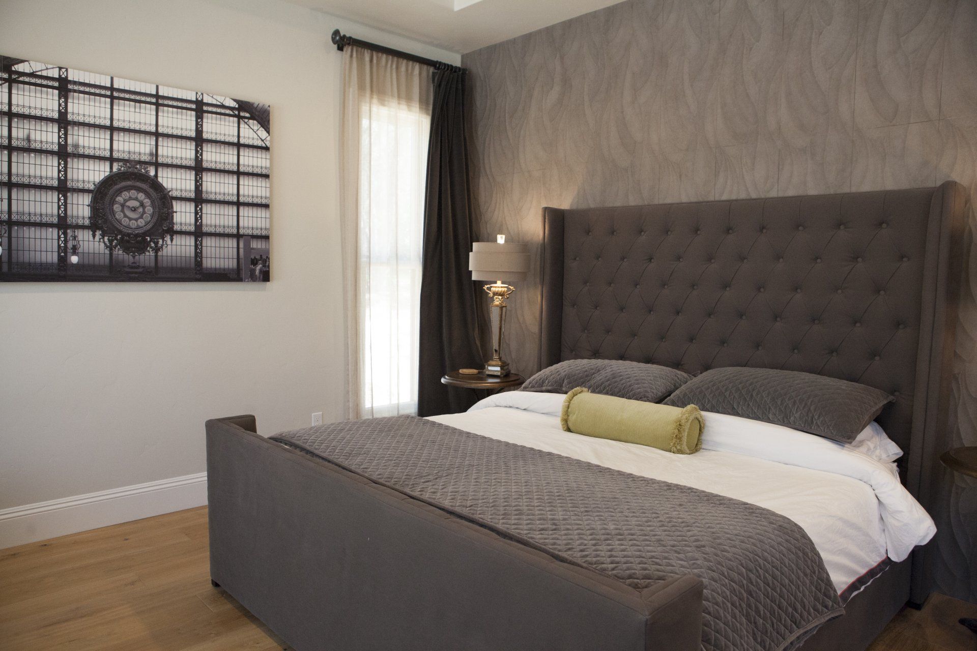 Bedroom with gray tufted headboard, matching bedding, and a framed art piece.