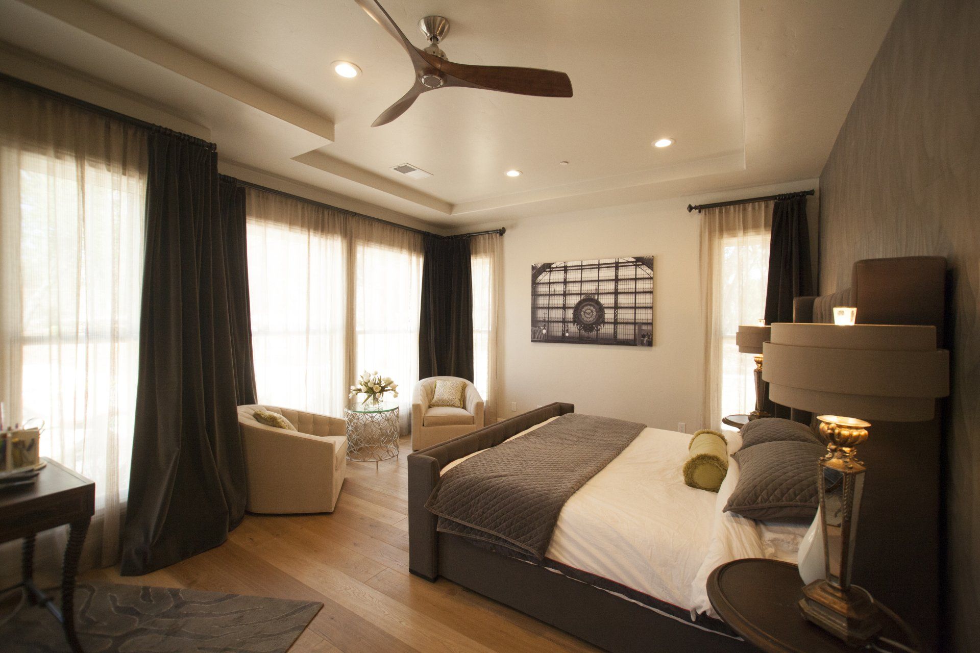 Elegant bedroom with dark curtains, wooden floor, and modern ceiling fan.