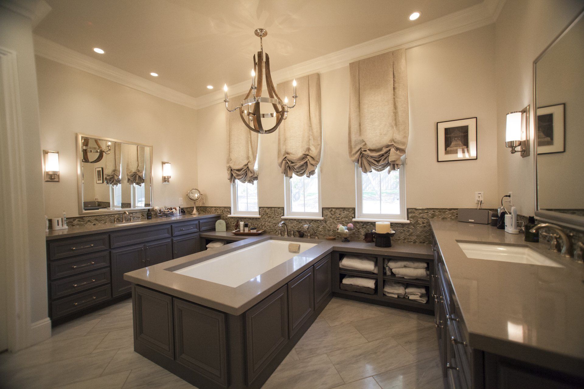 Luxurious bathroom with tub island, grey cabinets, marble floors, and chandelier.