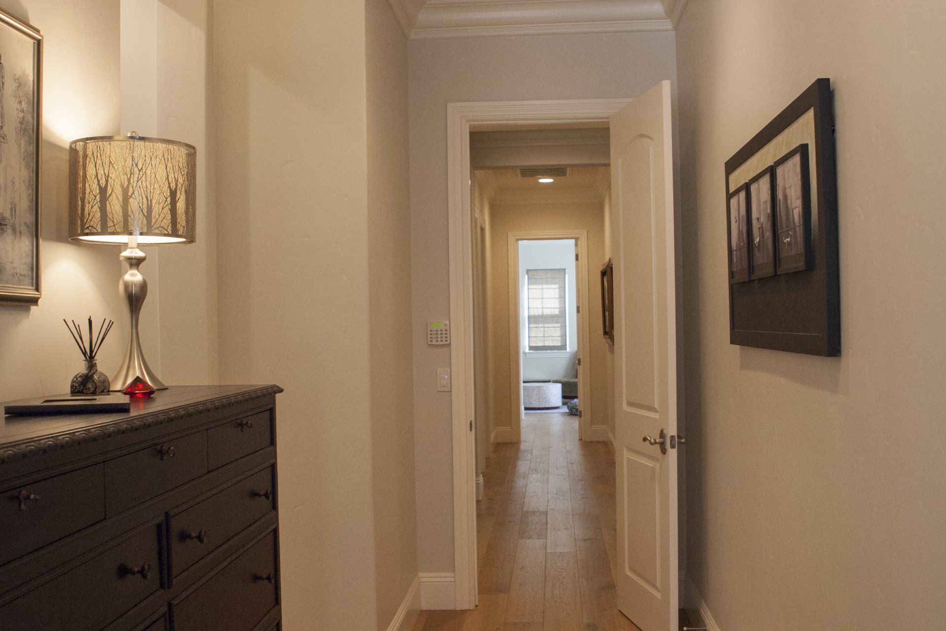 Narrow hallway with chest, lamp, and artwork; doorway at end.
