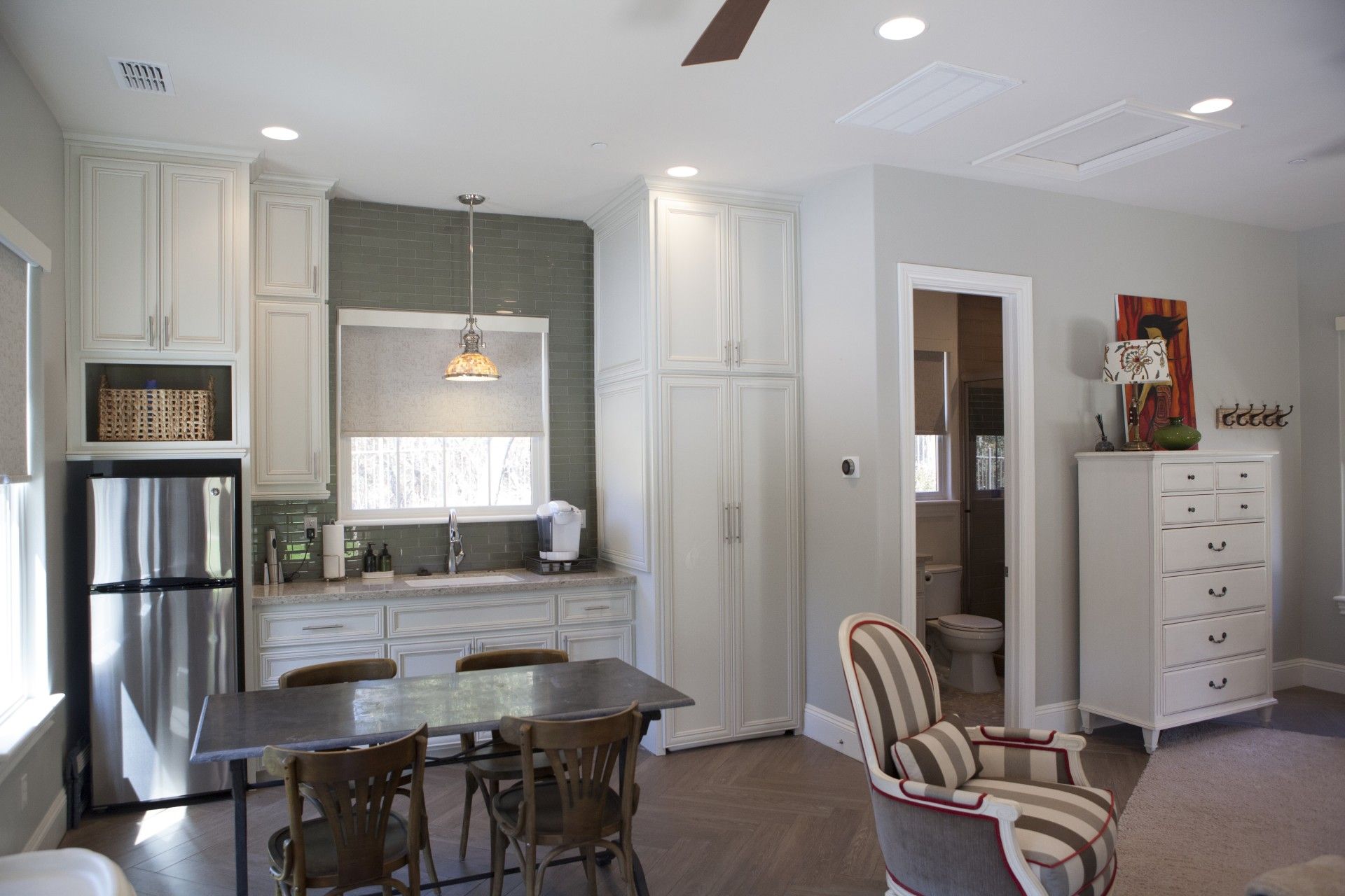Kitchenette with white cabinets, stainless steel fridge, dining table, and a striped armchair.