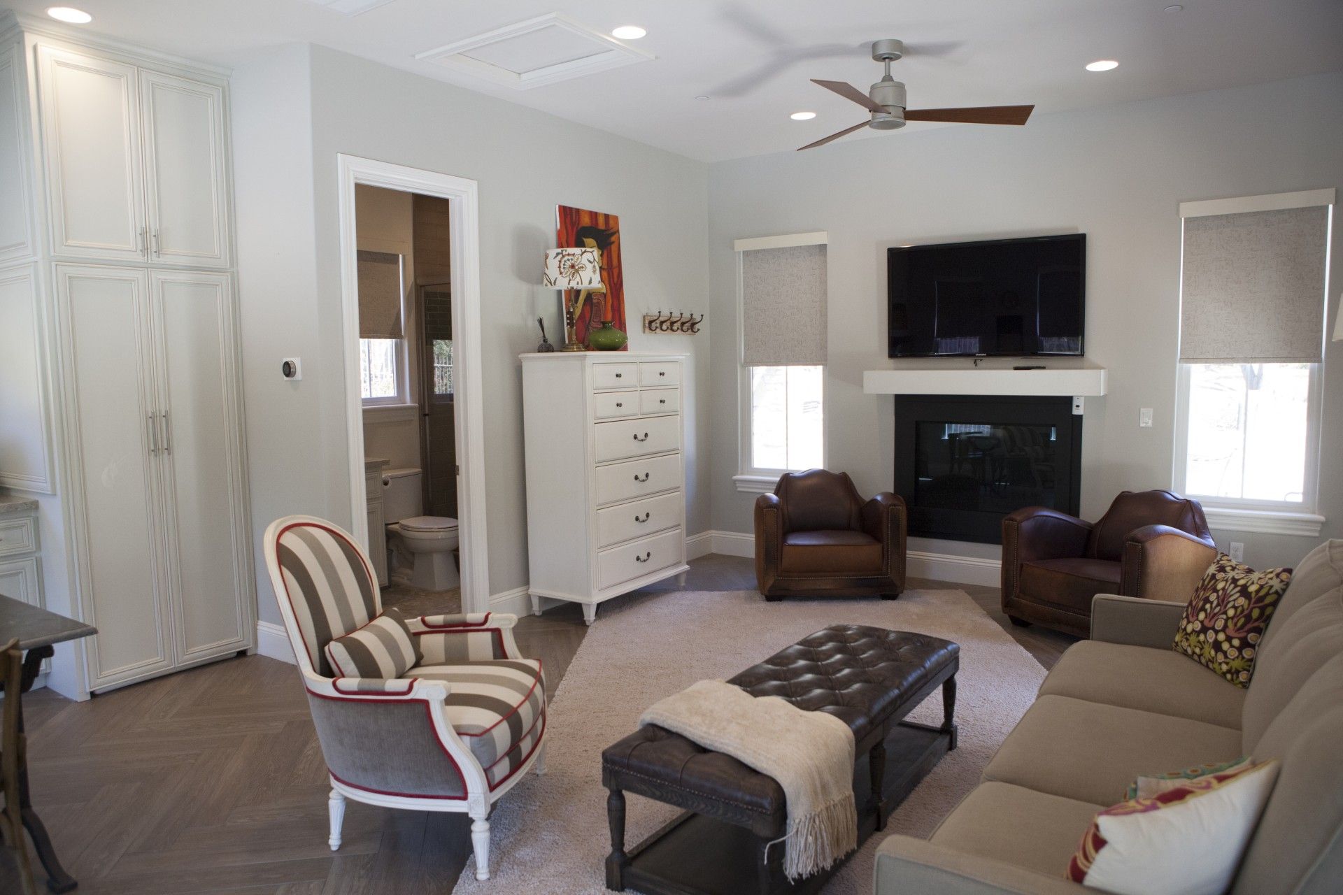 Spacious neutral-toned living room with fireplace, sofa, armchairs, and a patterned accent chair.