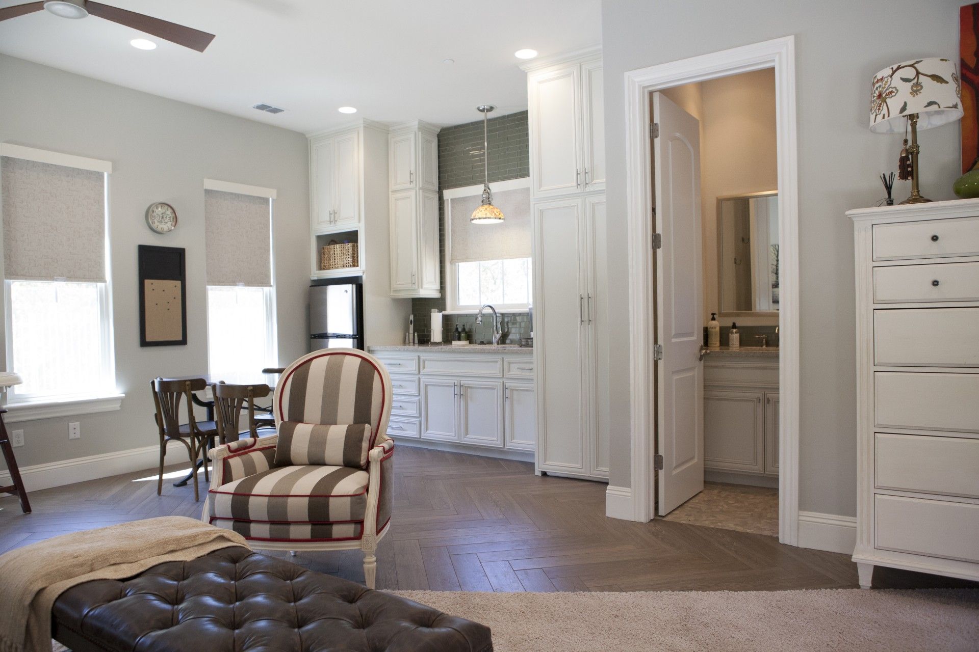 Open-concept living space with kitchen & bathroom visible; gray walls, white cabinets & wood floors.