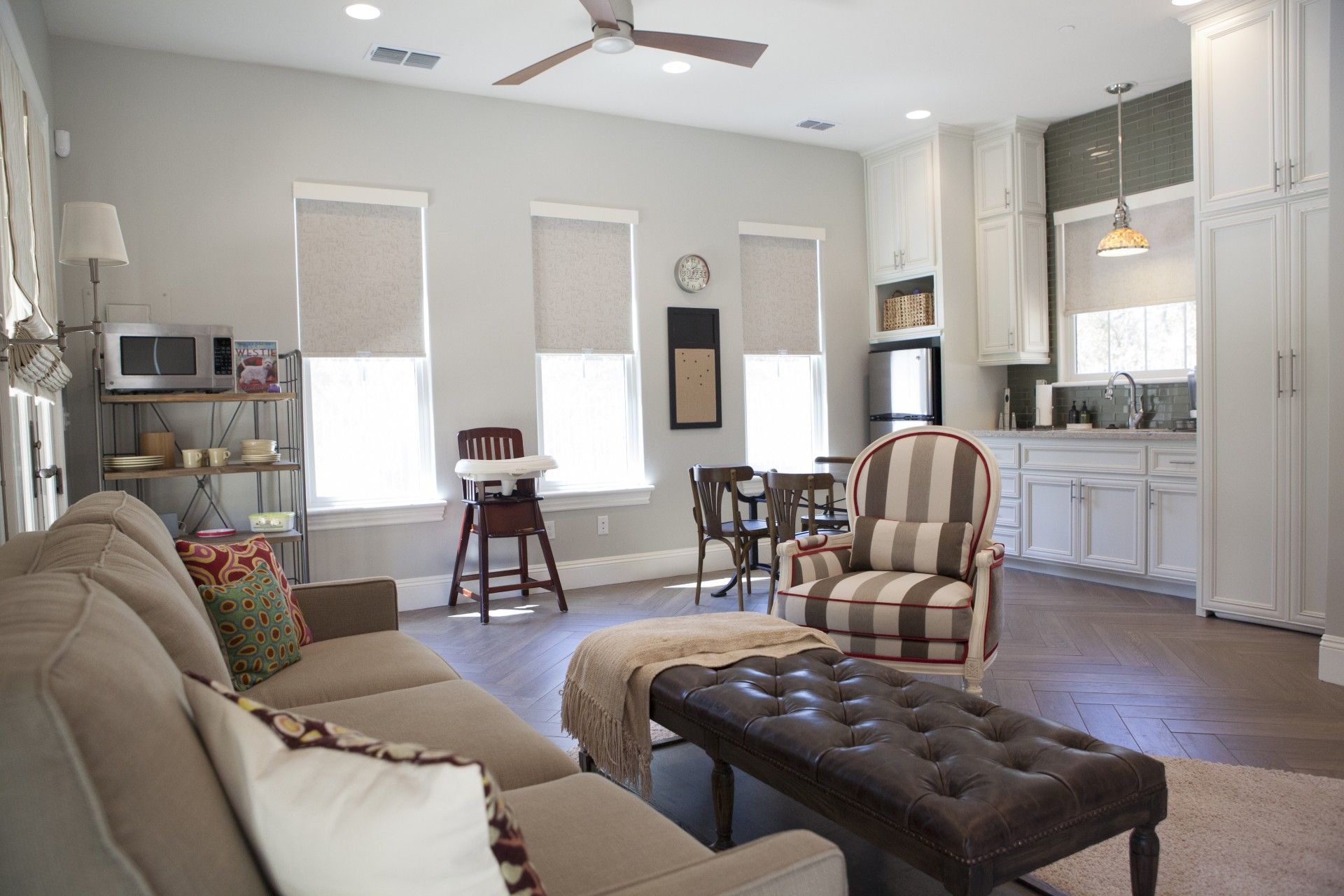 Living area with light gray walls, tan couch, and kitchen in the background.