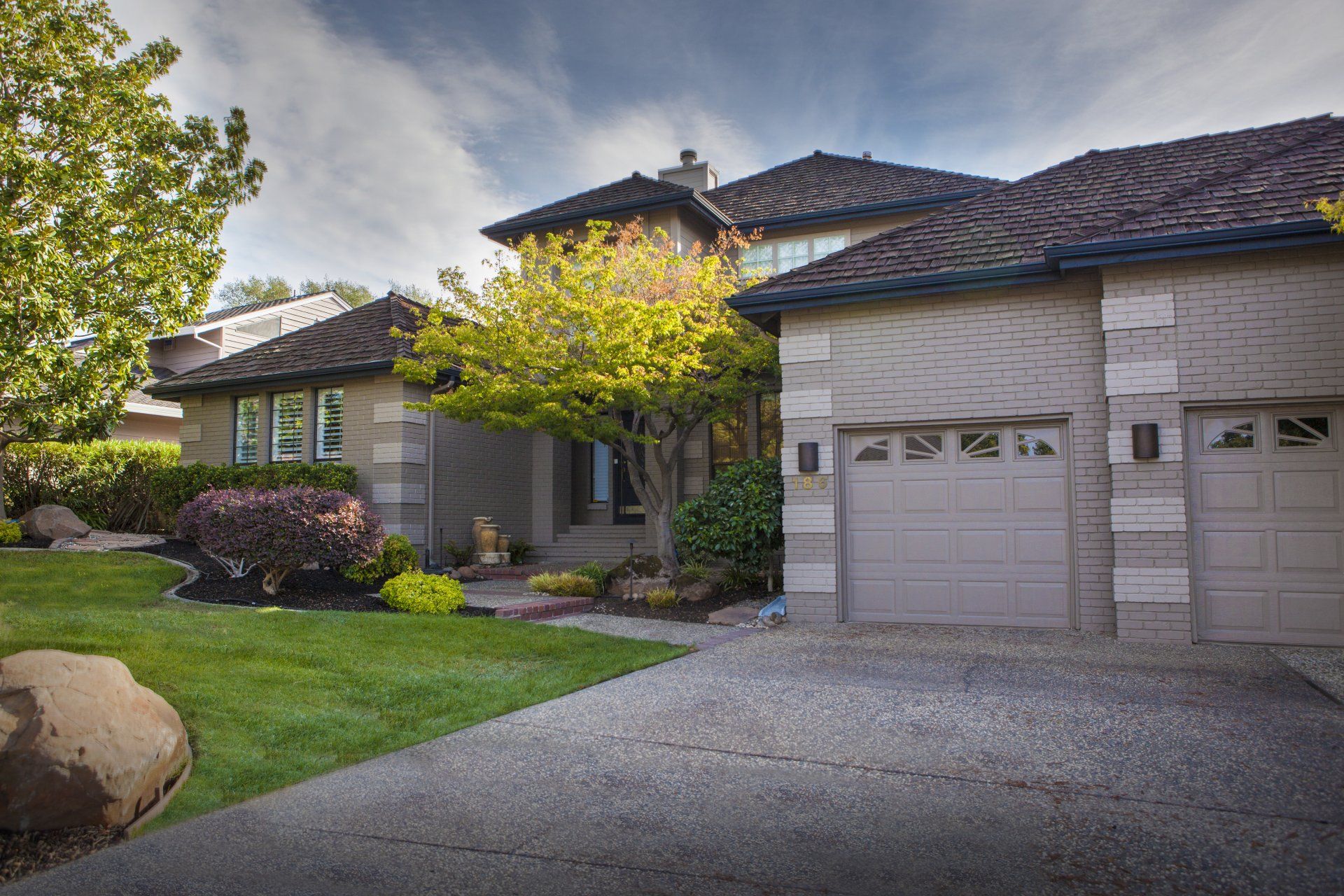 House with a gray facade, two-car garage, and green lawn; a tree shades the front entrance.