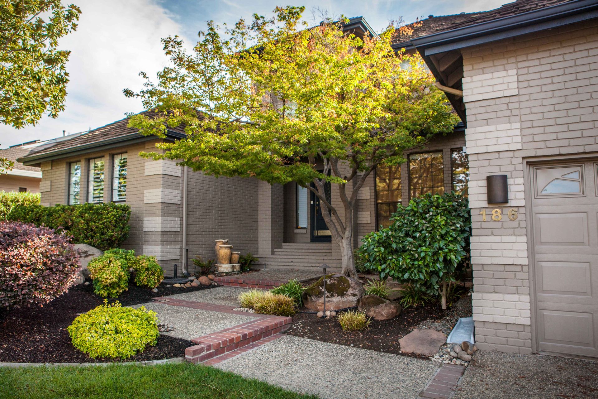 House exterior with brick facade, trees, and a path leading to the front door.