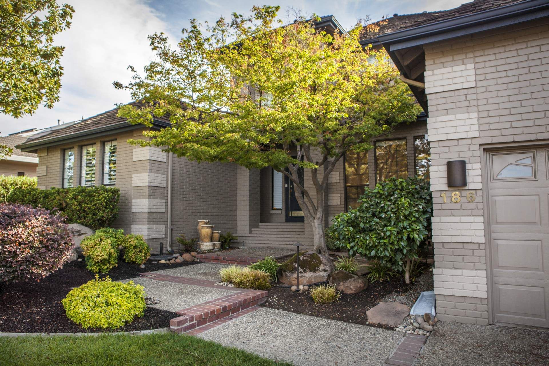 House exterior with landscaping, featuring a tree, brick pathway, and garage.