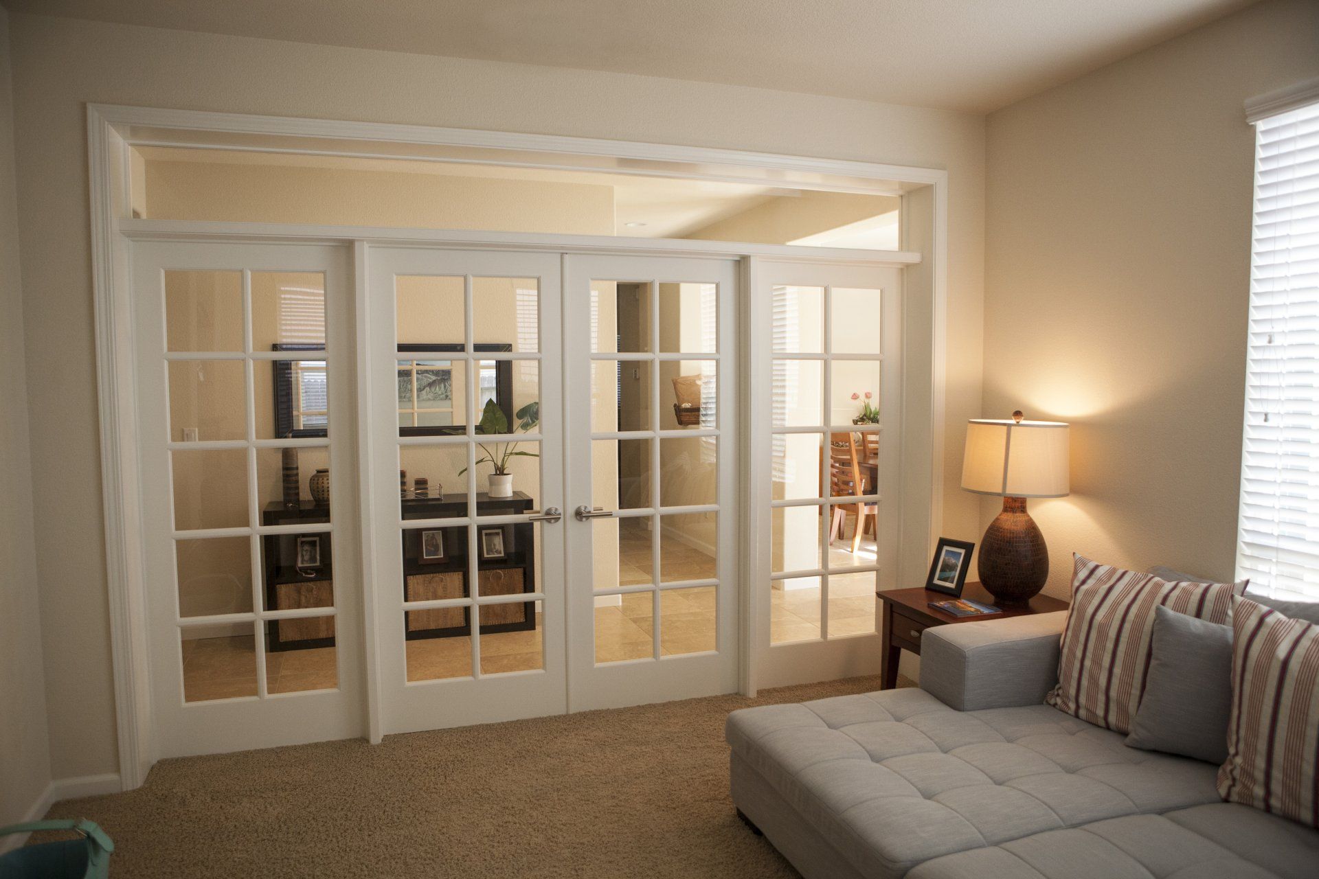 Glass-paned French doors between rooms; a sofa in the foreground, table with lamp and art.
