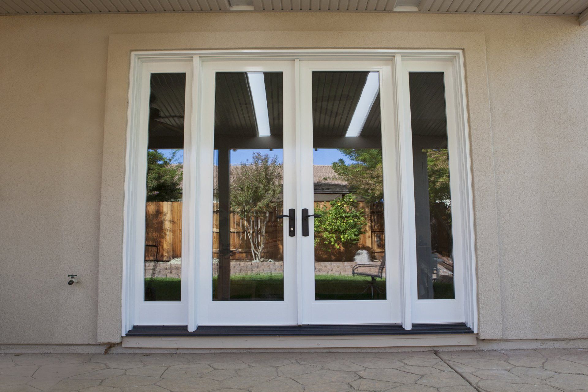 White French doors with glass panels, in a stucco wall, leading to a backyard.