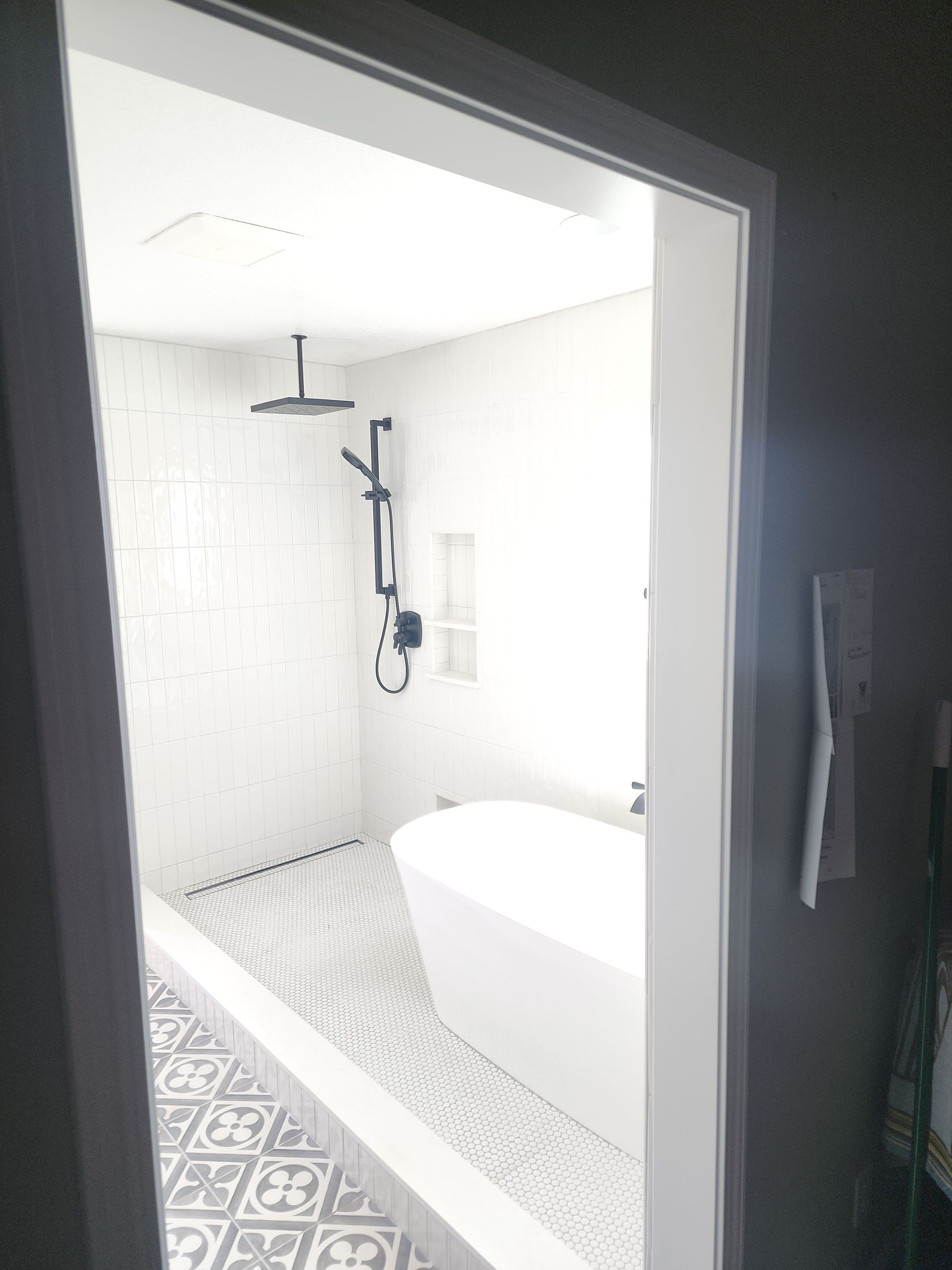 Bathroom with white tile walls, a black shower fixture, a freestanding tub, and patterned floor.