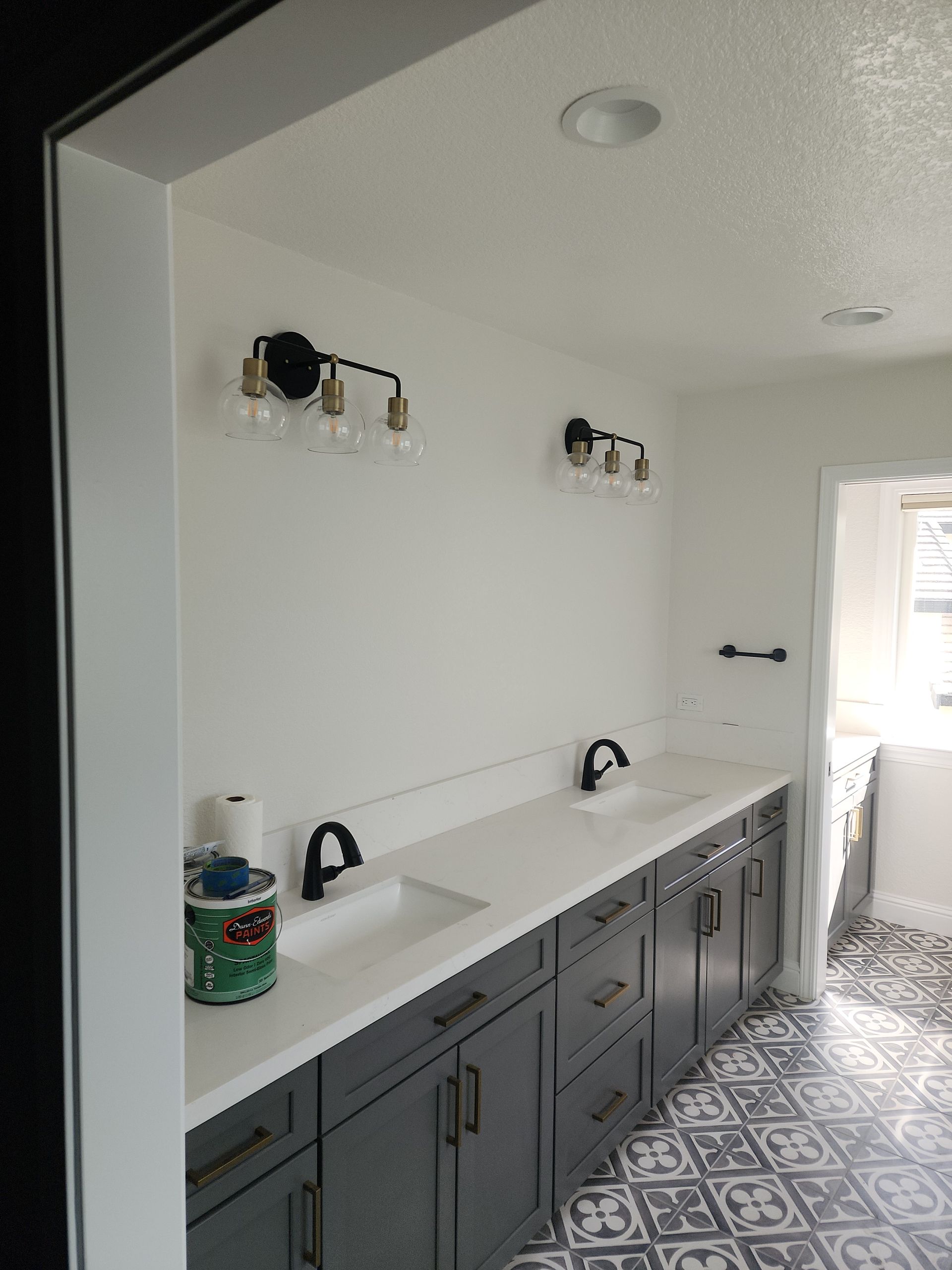 Bathroom with double vanity, gray cabinets, white countertop, black fixtures and lighting, and patterned floor.