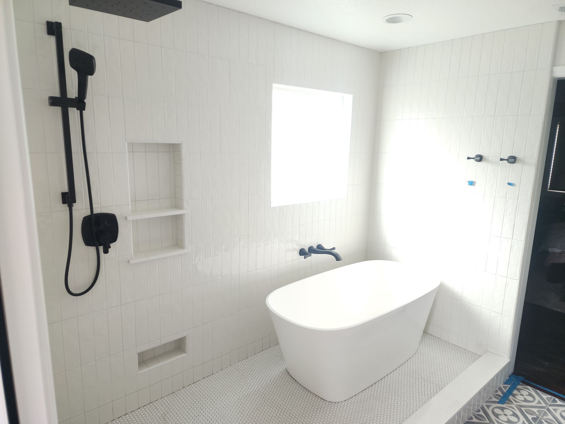 Bathroom with white tile, a soaking tub, and black shower fixtures.