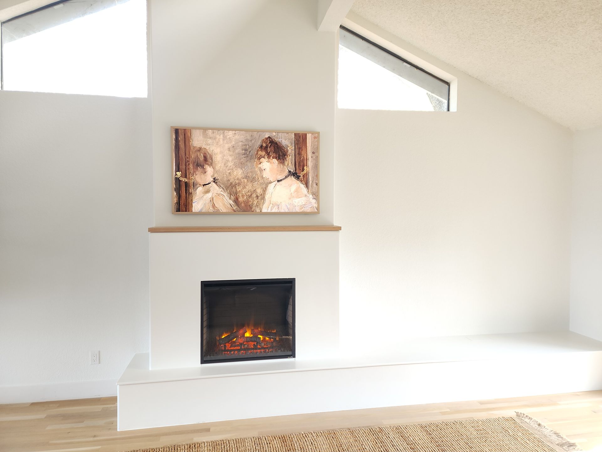 White fireplace with art and angled windows in a bright room.
