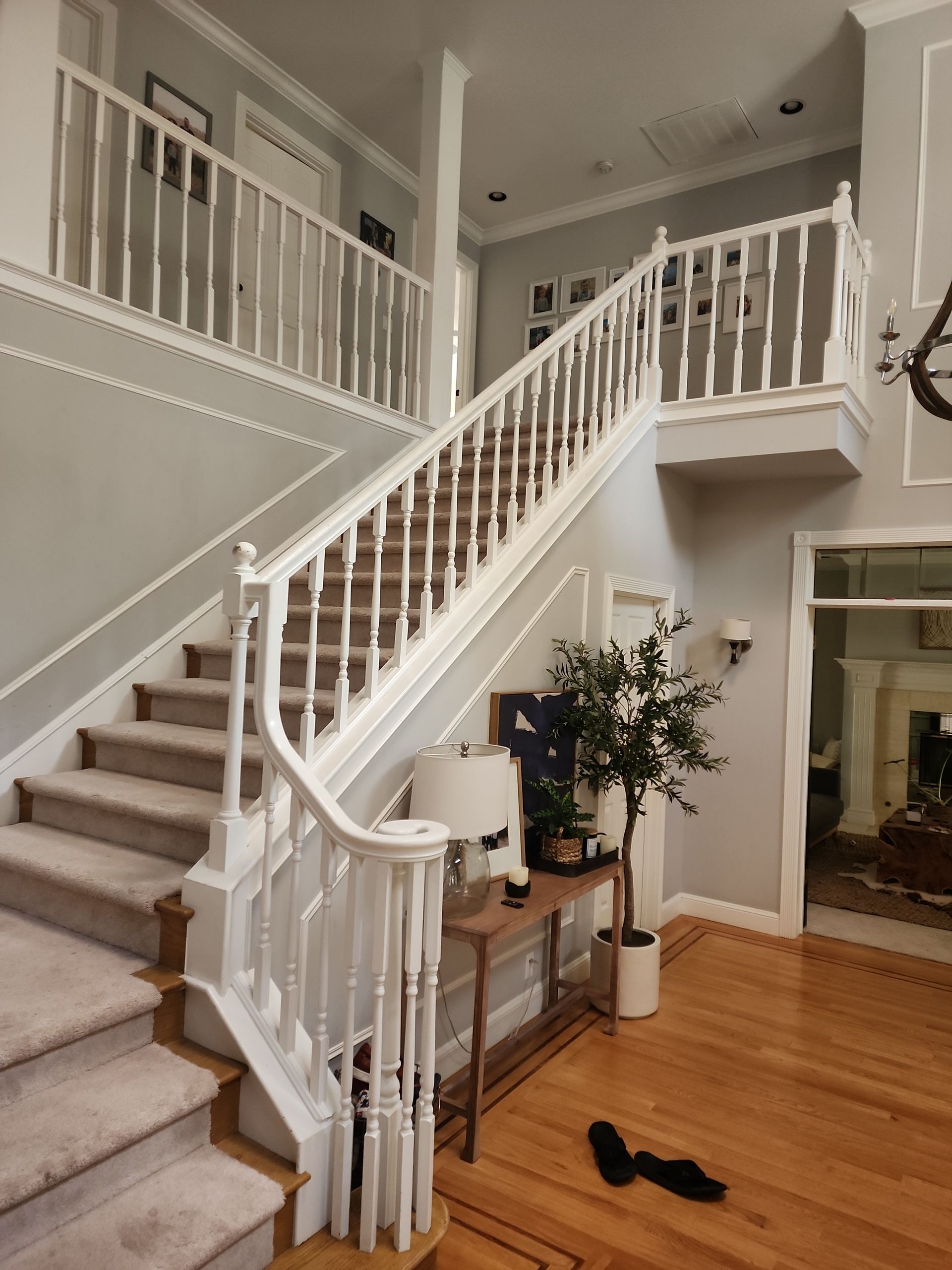 Two-story foyer with a staircase and landing. White balustrades, wooden floors, and light gray walls.