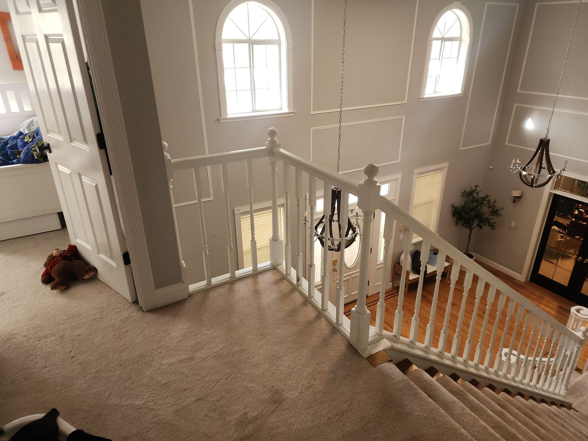 Interior view: a two-story foyer with a staircase, white railing, high windows, and a chandelier.