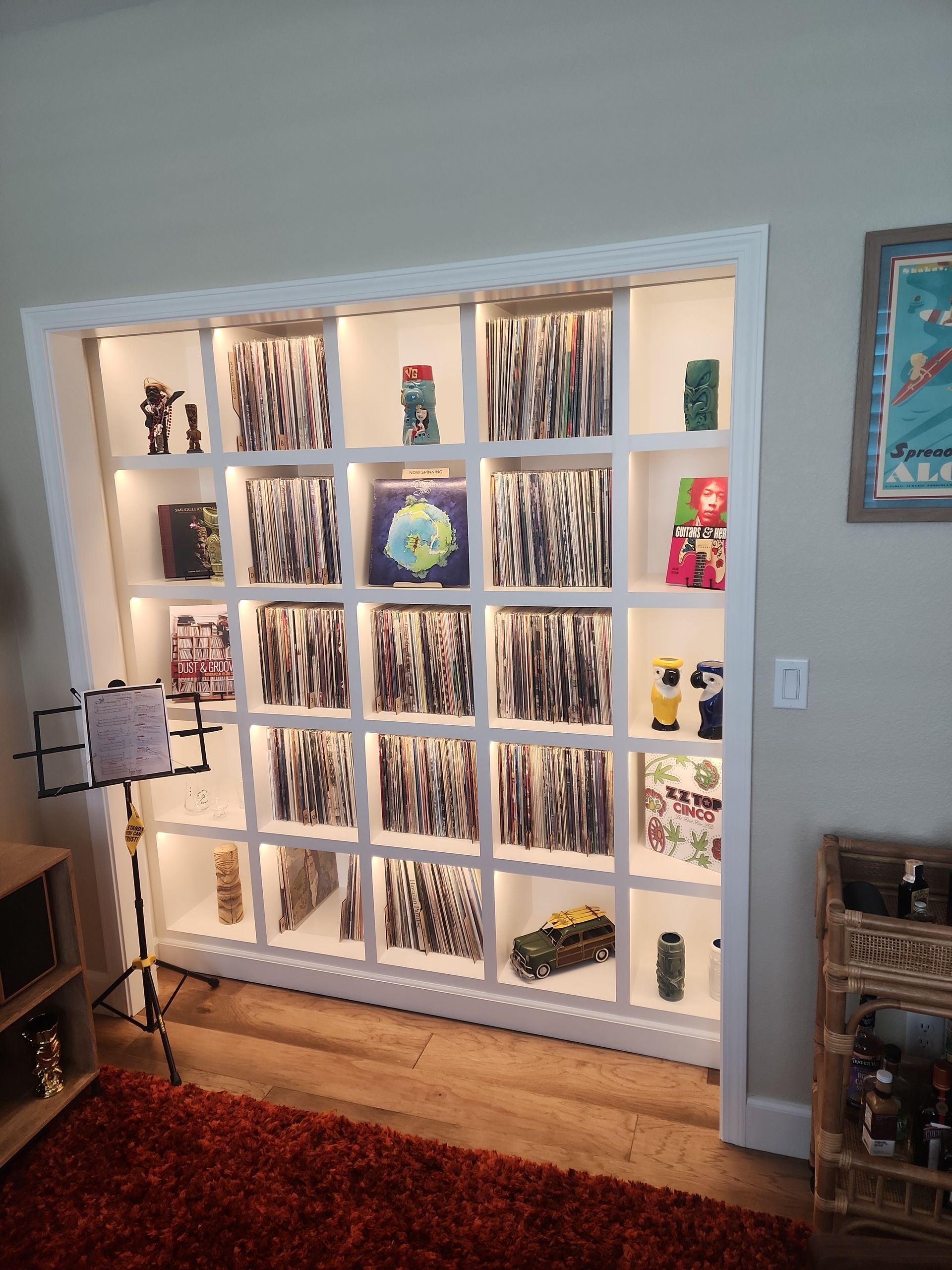 Built-in white shelving unit with vinyl records and decorative items; lit with warm lights, on a wood floor.