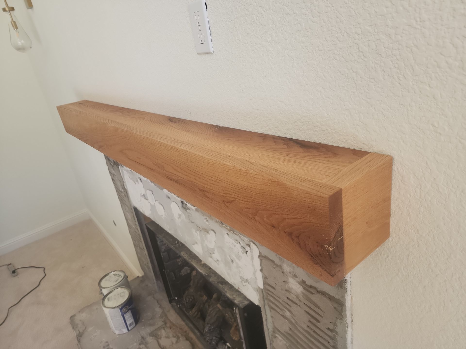 Wooden fireplace mantel over a fireplace, against a white wall.