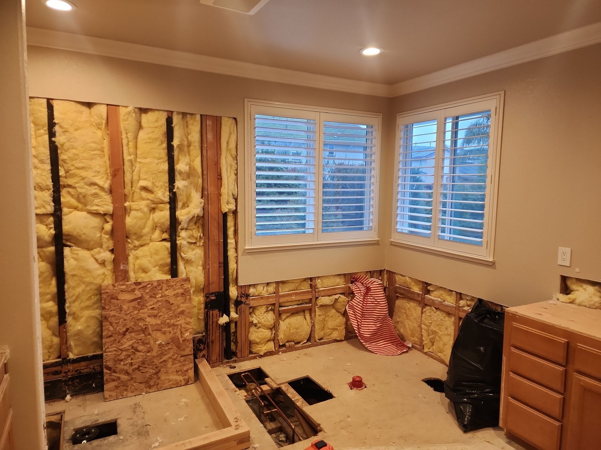 Bathroom undergoing renovation with exposed insulation, framing, and a window with shutters.