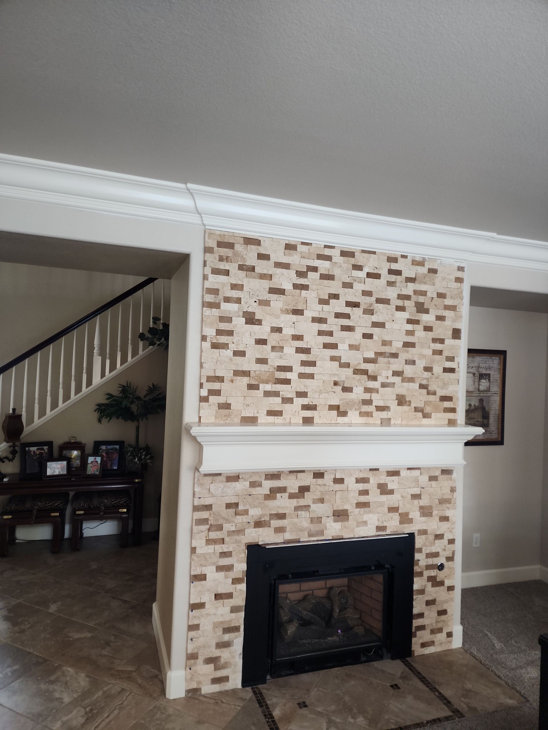 Fireplace with textured stone facing, white mantel, black fireplace insert, and a view of stairs.
