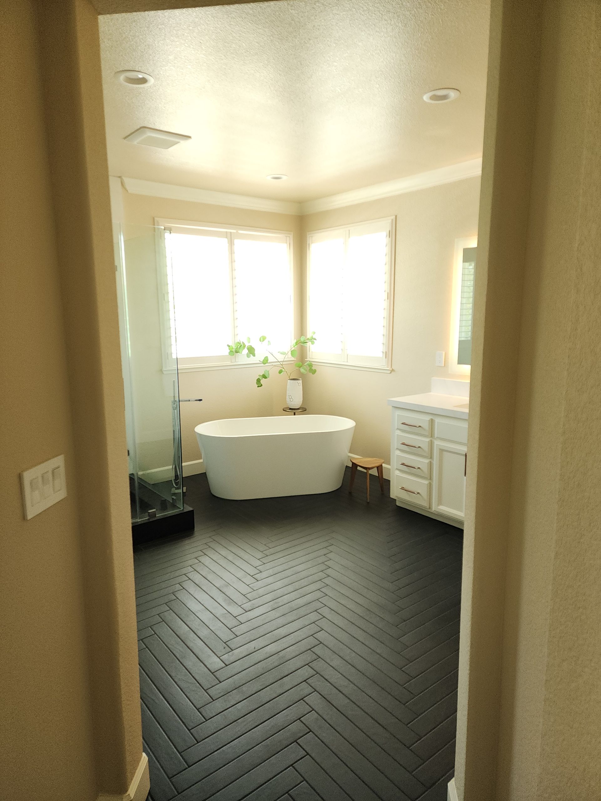 Bathroom with black herringbone floor, white tub, vanity, and windows.