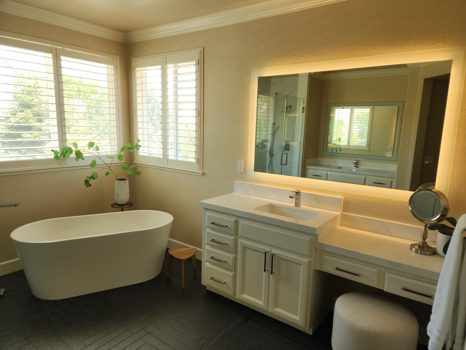 Bathroom with a white soaking tub, vanity, and large mirror with warm lighting.