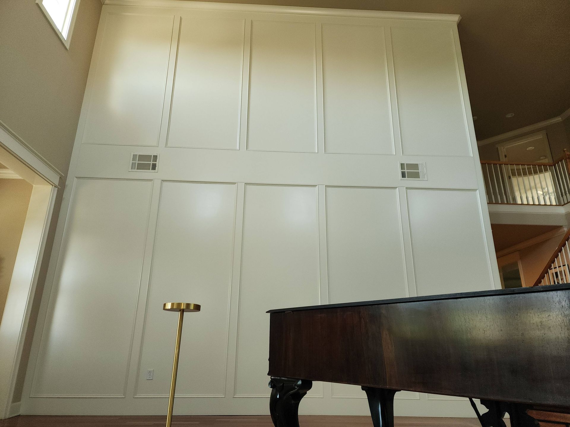 White paneled wall in a home with a grand piano in front.
