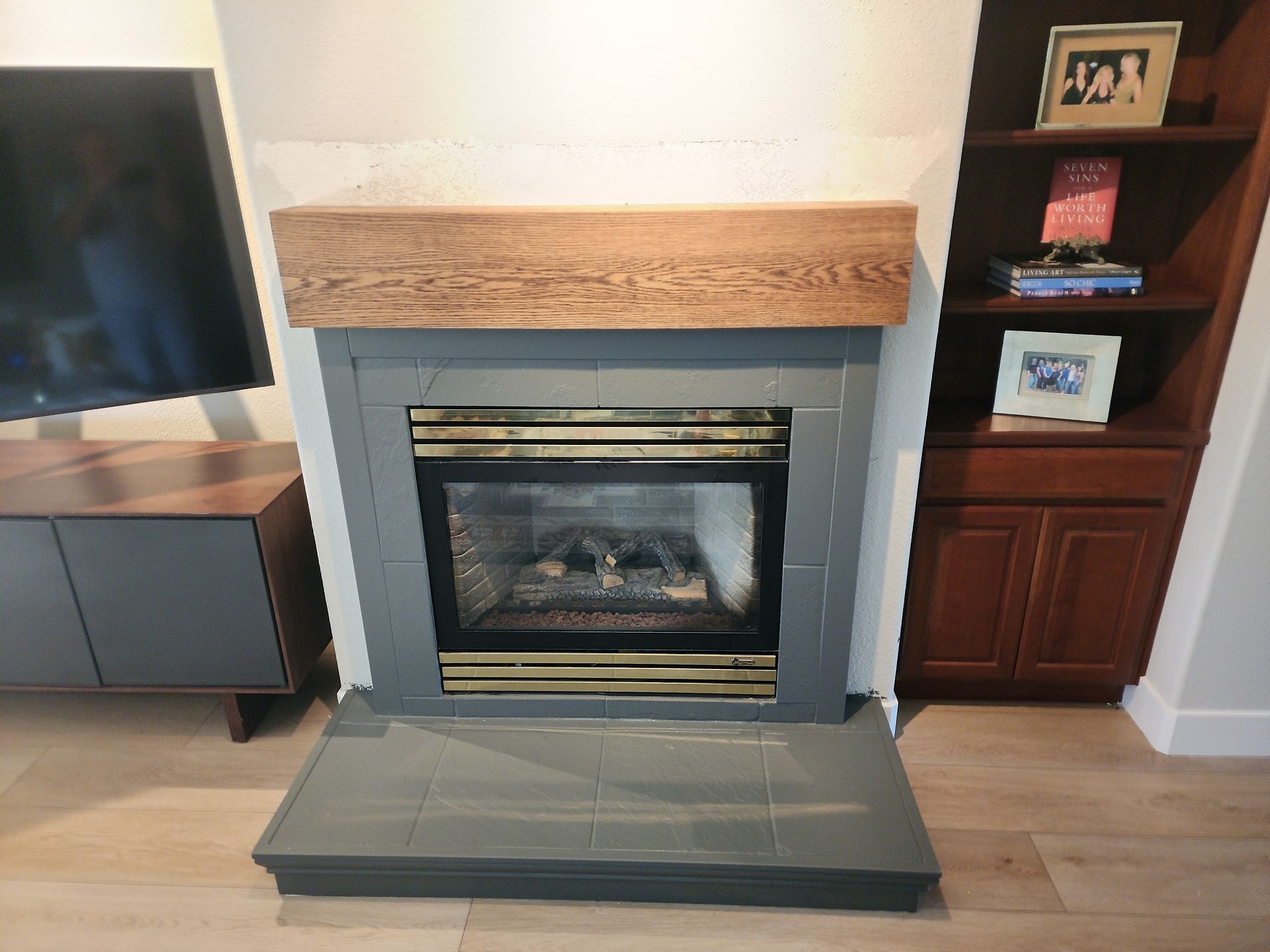 Fireplace with gray tiles, wooden mantel, and built-in wooden shelves.