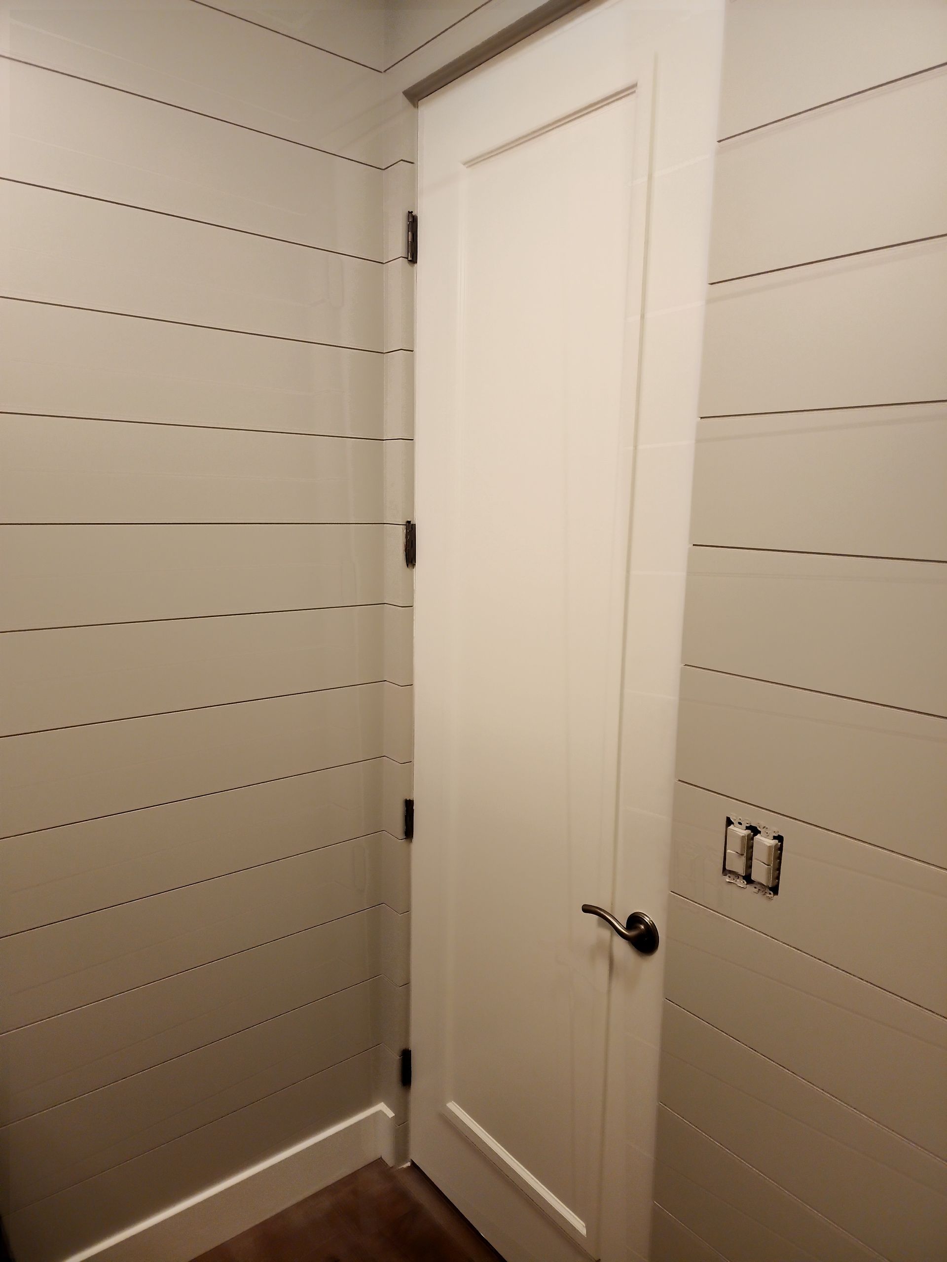 White door in a corner, with horizontal lines on the walls. Dark doorknob and light switches.