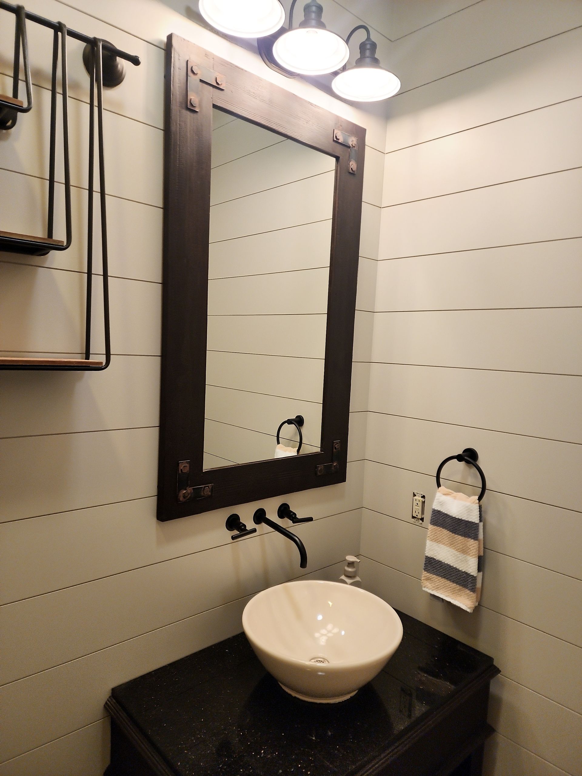 Bathroom with a dark vanity, vessel sink, and a dark-framed mirror. Greenish walls, black faucet and towel ring.