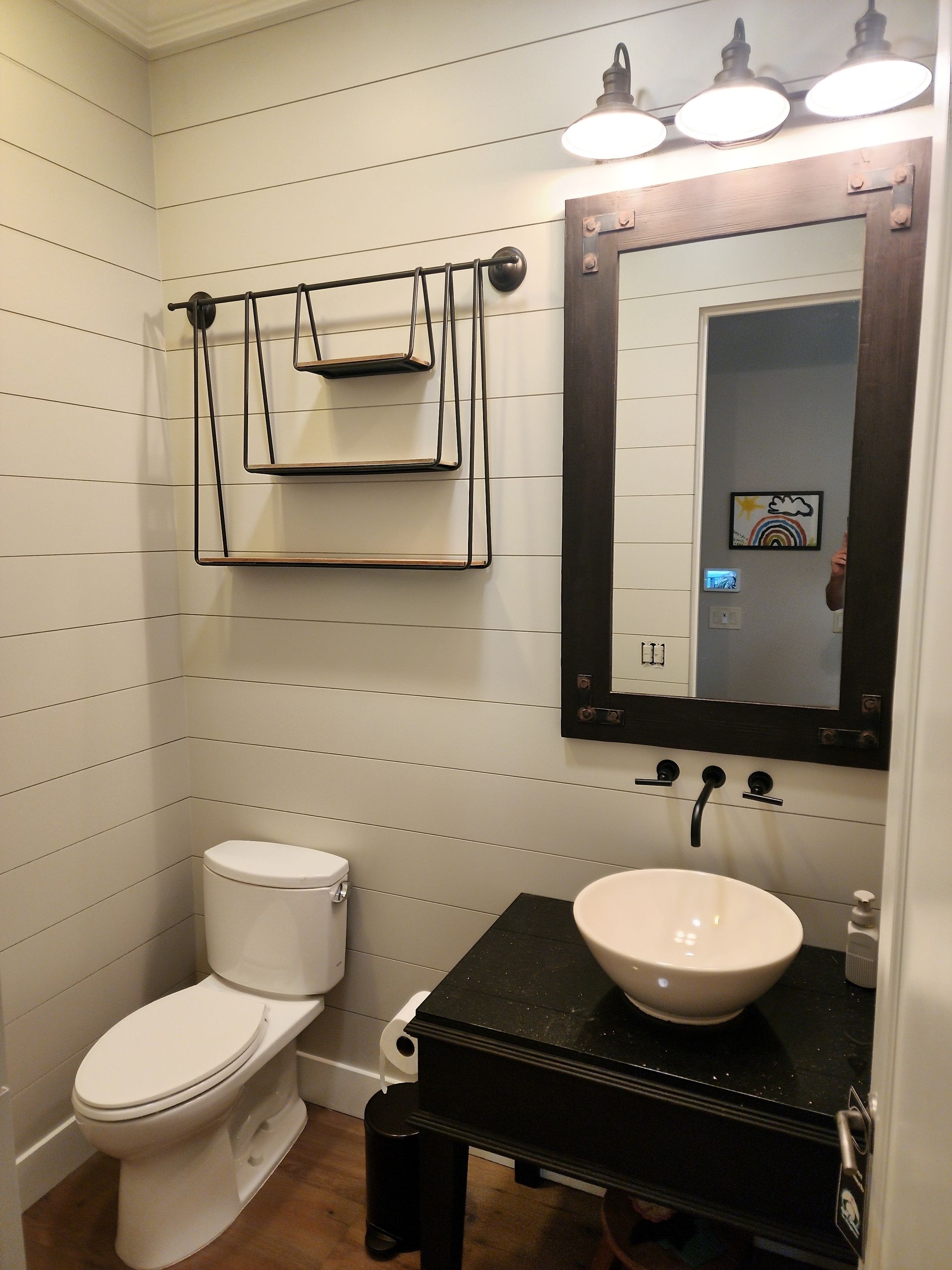 Small bathroom with toilet, sink, and mirror, with wood and metal decor.