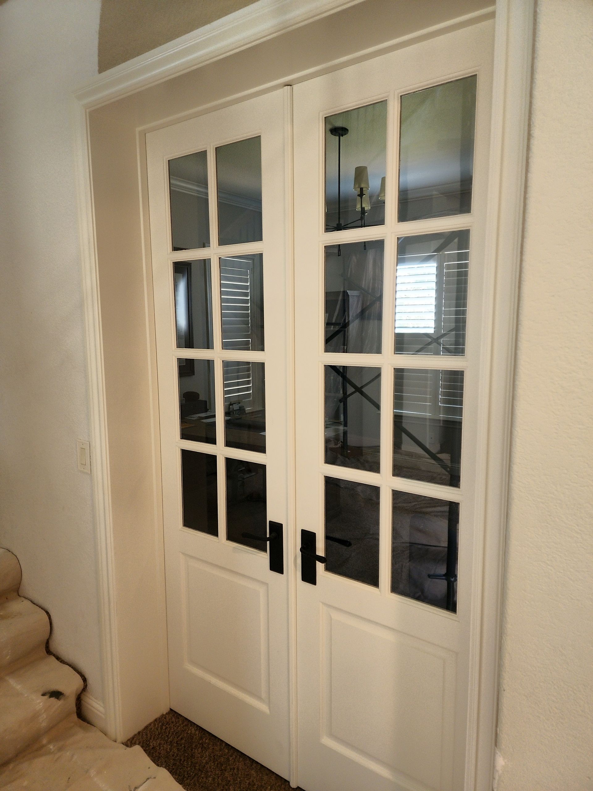 Pair of white French doors with glass panels, black handles, and a neutral-colored door frame.