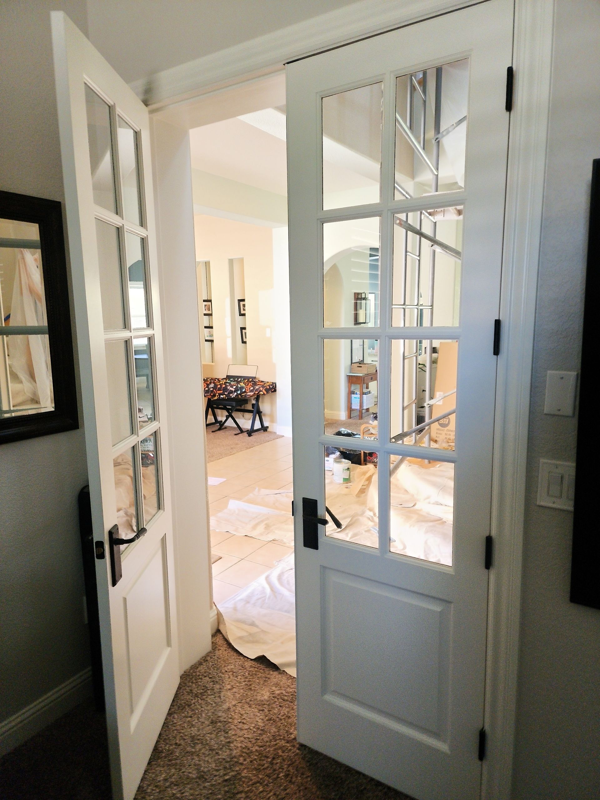 French doors open to interior room with work in progress; white doors with glass panes.