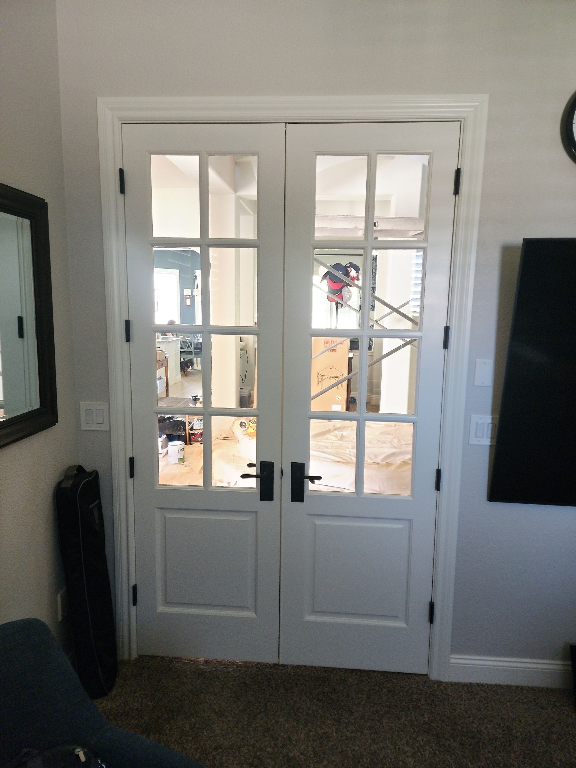 White French doors with black hardware, in a room with a mirror and a television.