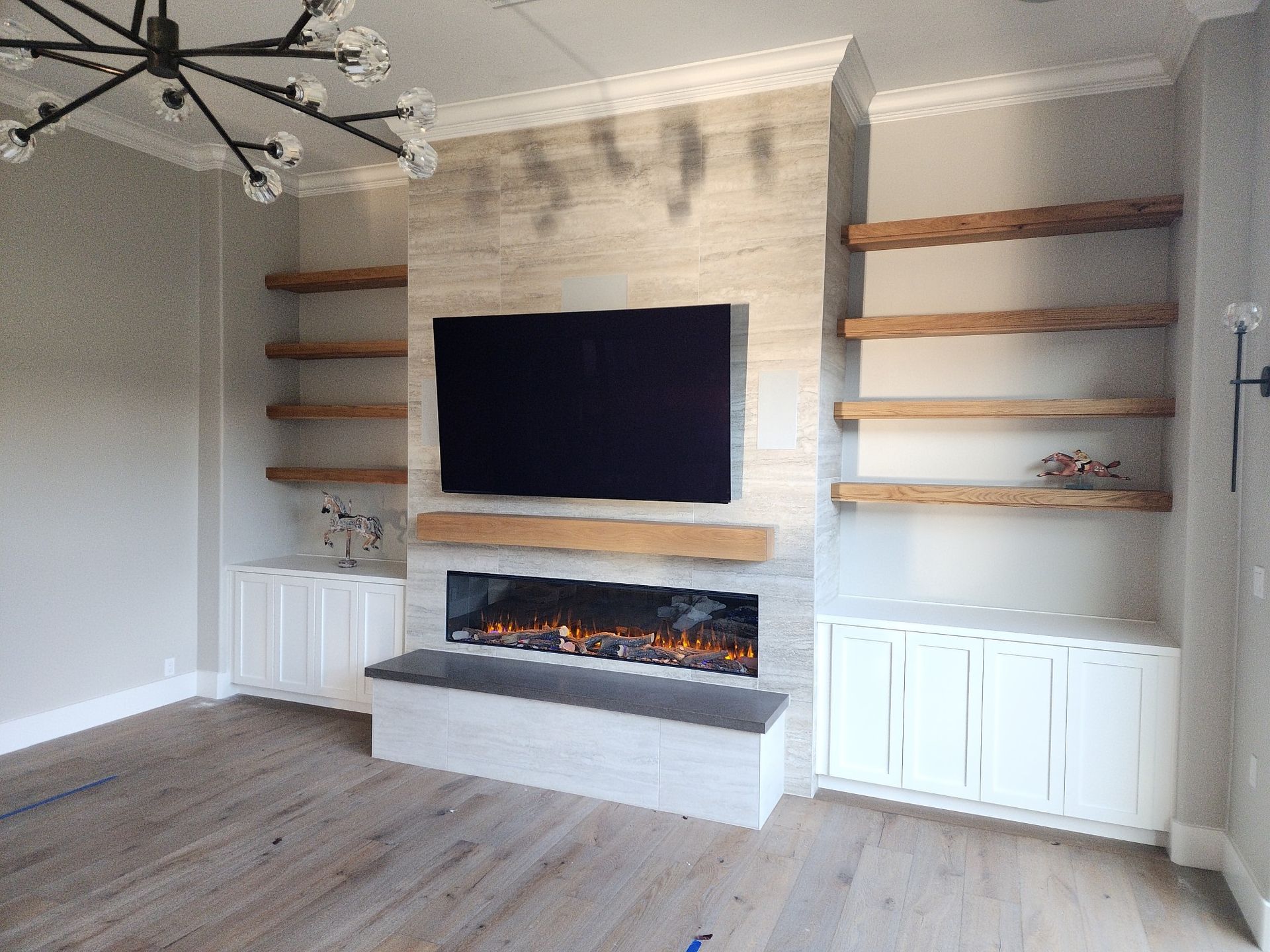 Living room with fireplace, built-in shelving, TV, and white cabinets against light stone wall and hardwood floor.