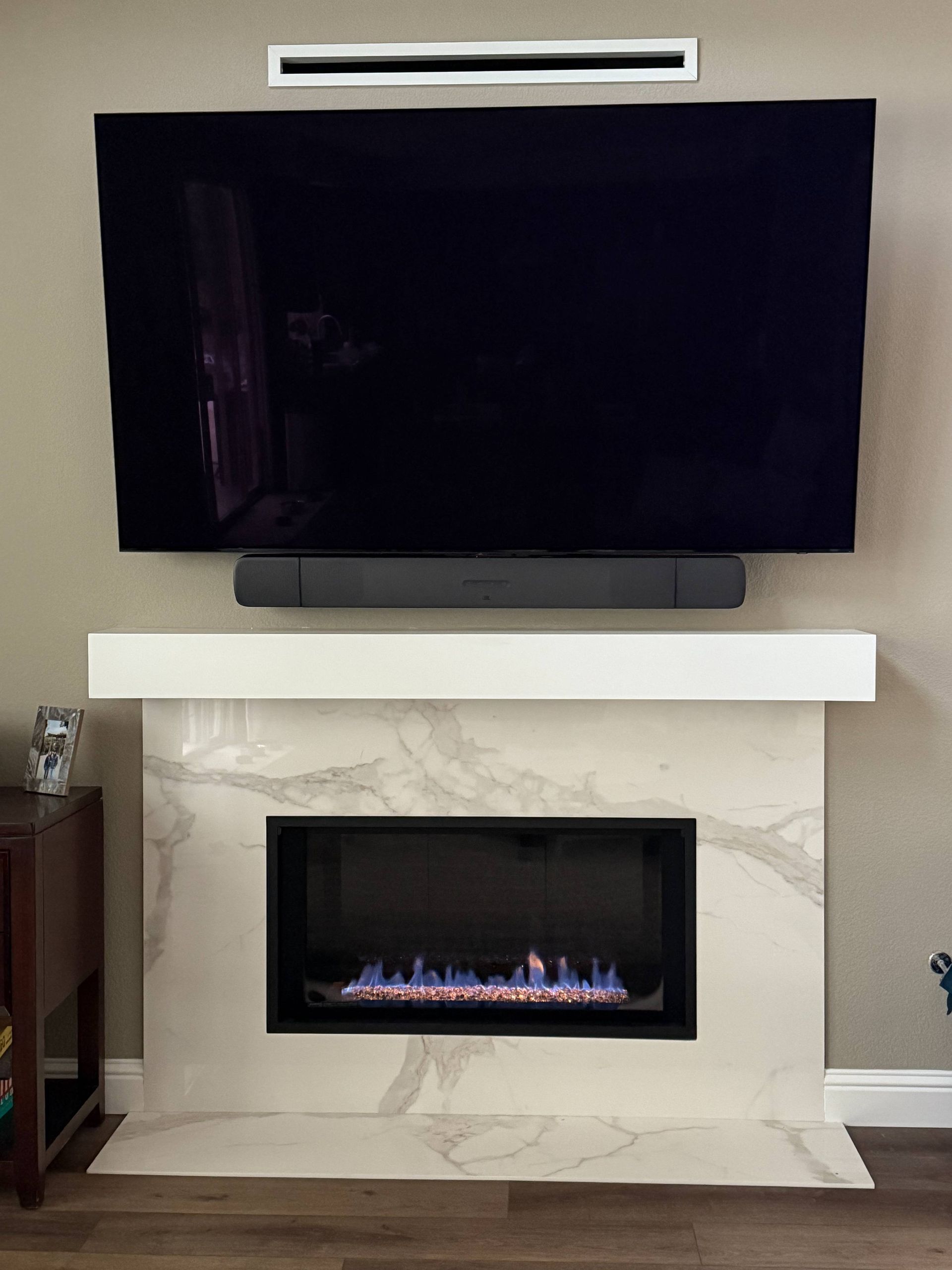 Fireplace with a TV, soundbar, and vent above. White marble surround.