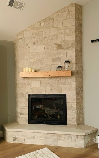 Stone fireplace in a corner, featuring a black firebox, wooden mantel with candles, and a light-colored stone hearth.