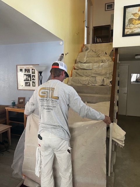 Man in paint clothes covering stairs with protective plastic. Indoor setting.