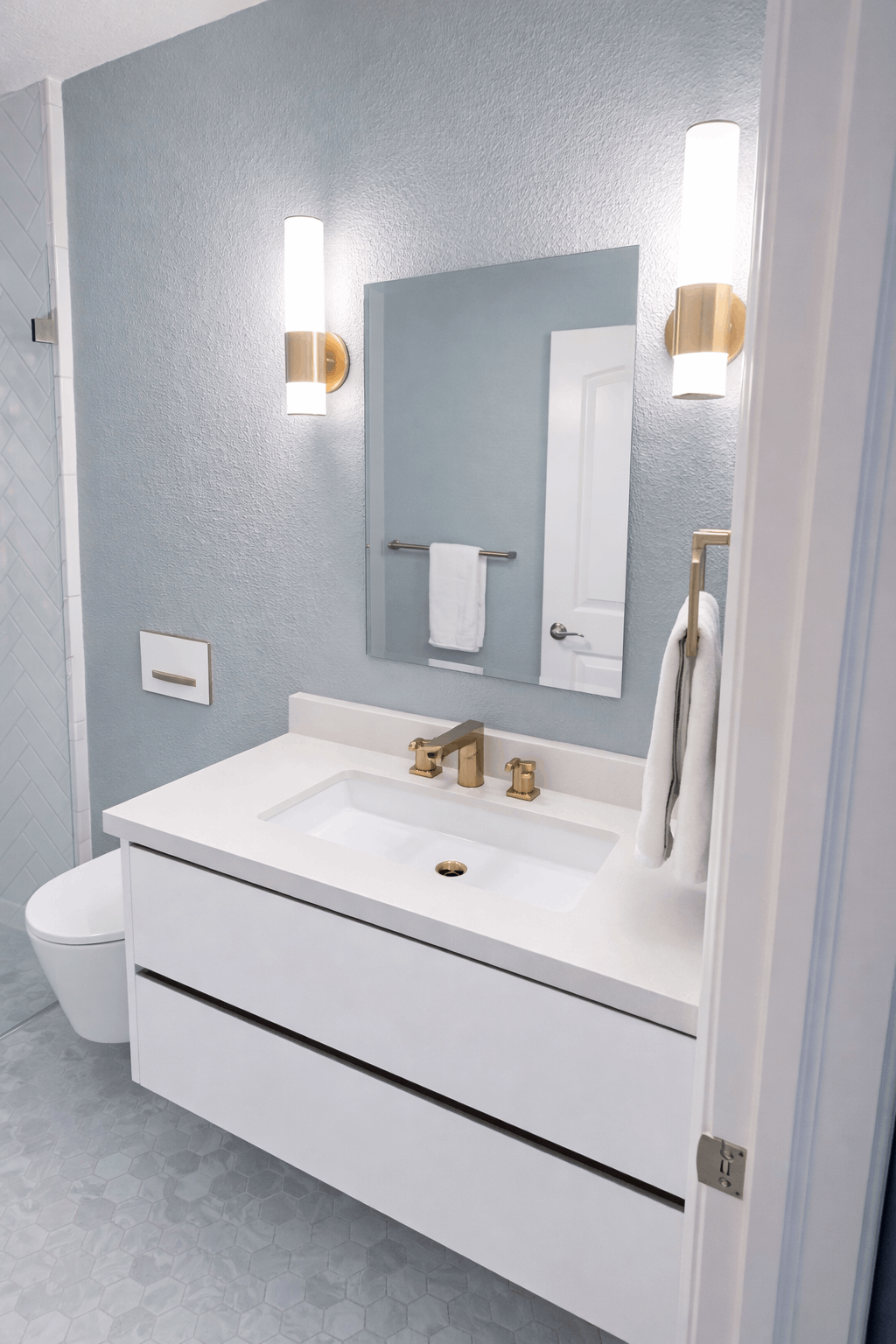 Modern bathroom with a white vanity, gold fixtures, and blue textured walls.