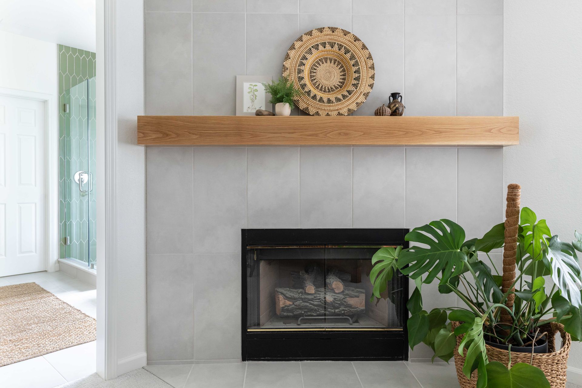 Fireplace with wood shelf, woven decor, and a monstera plant in a wicker basket.