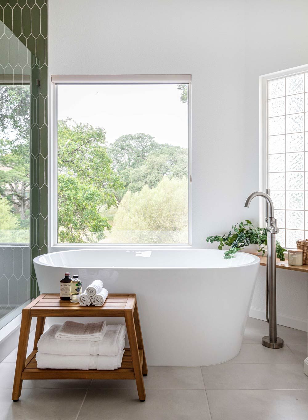 White modern bathroom with a freestanding tub in front of a large window with a wood bench.