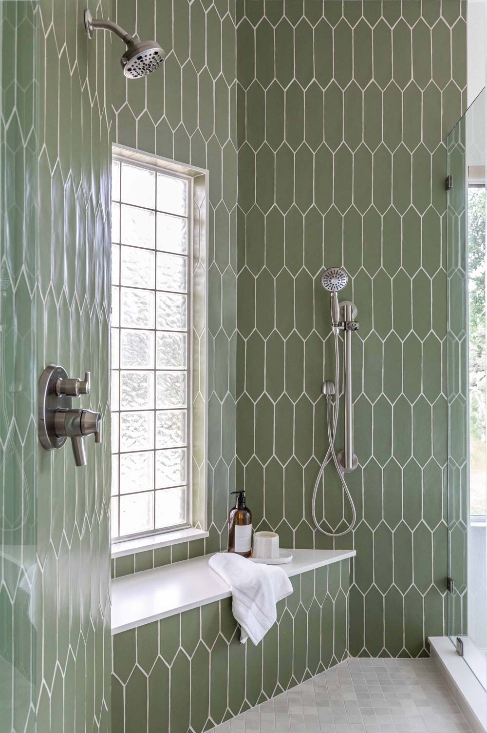 Green tiled shower with window, shelf, and silver fixtures.