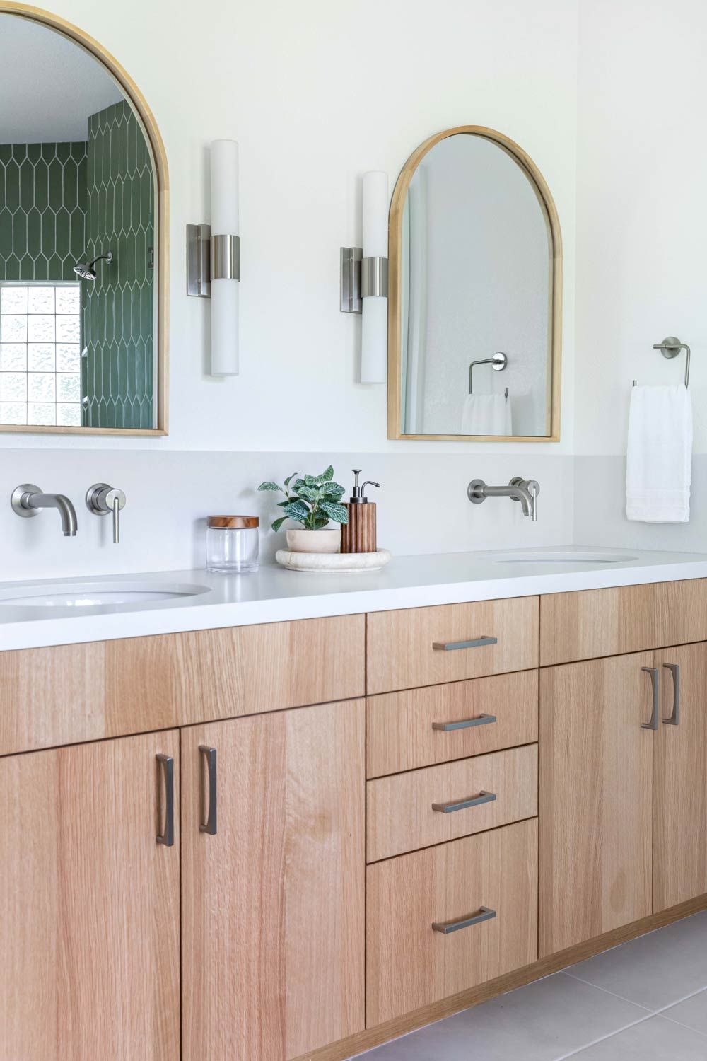 Bathroom with wood vanity, arched mirrors, and wall-mounted faucets. Neutral tones with green tile accent wall.