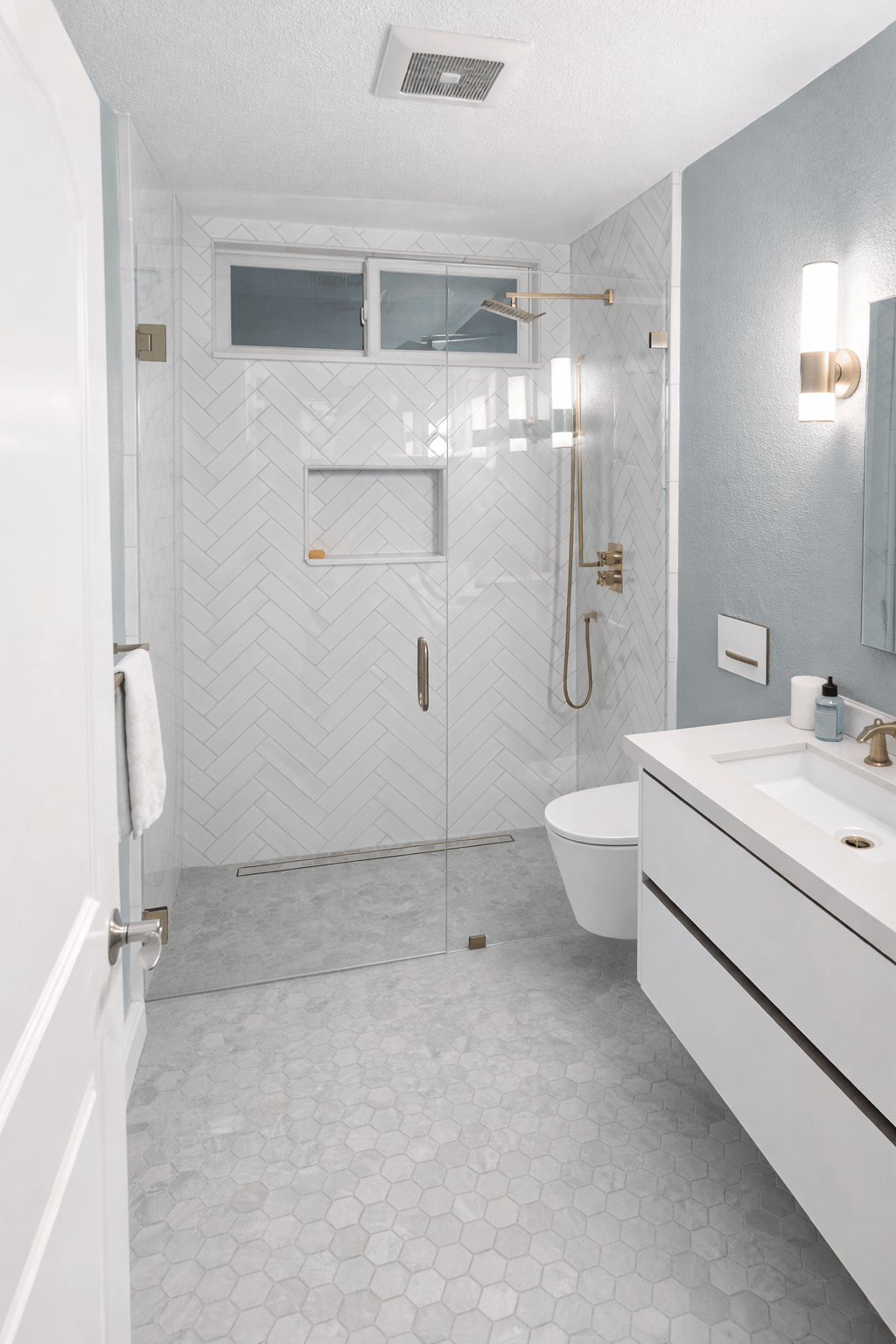 Modern bathroom with white and gray tile, glass shower, and floating vanity.