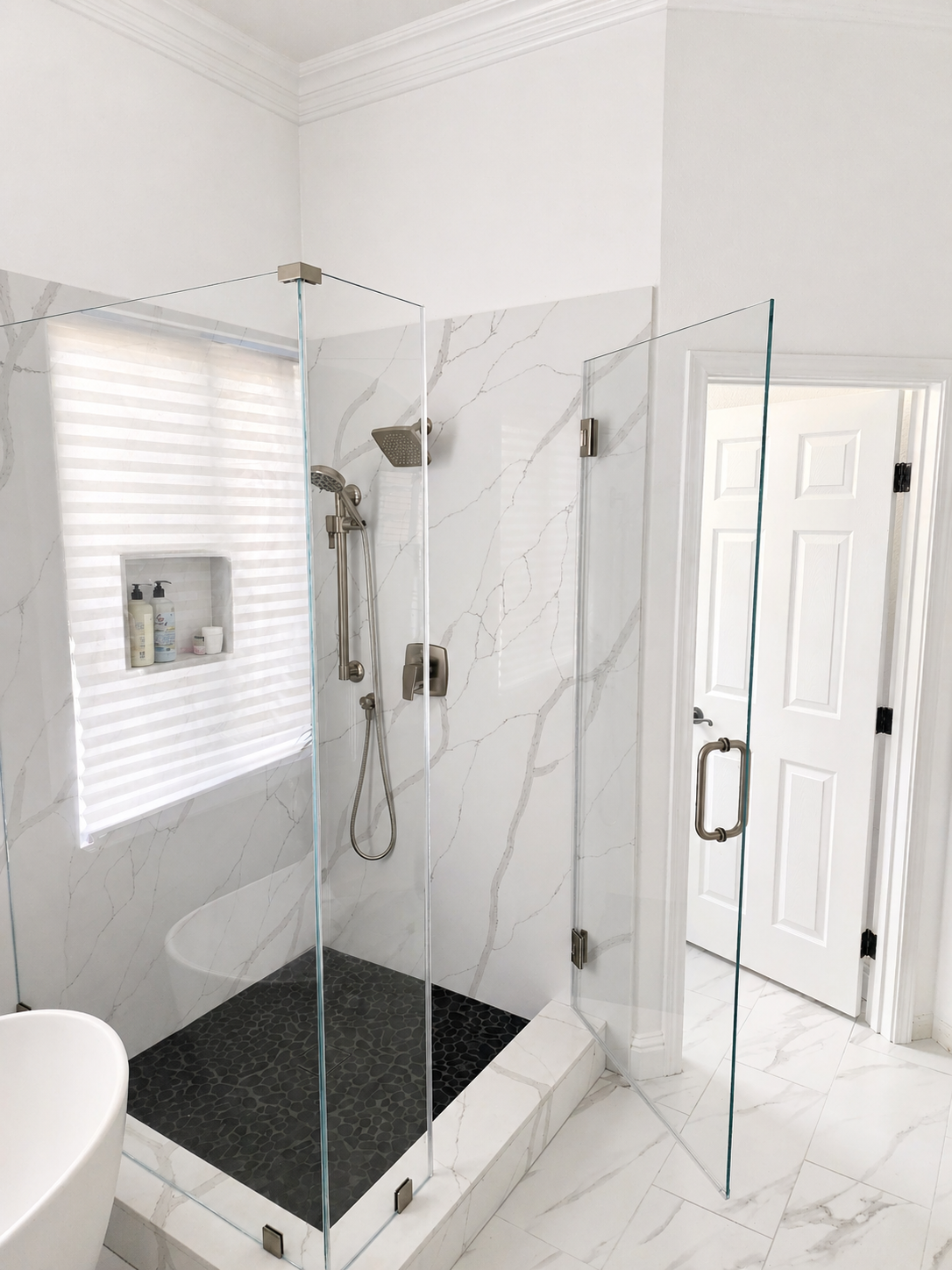 Modern white bathroom with glass-enclosed walk-in shower and black shower floor tile